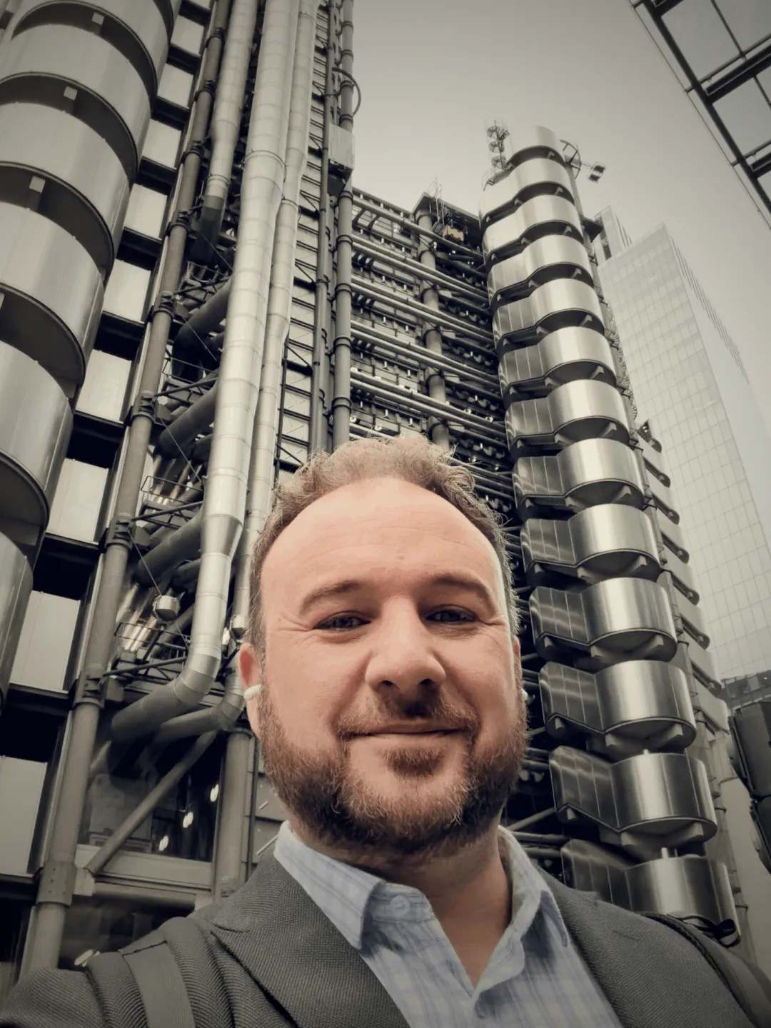 Joe Braidwood outside the Lloyd&rsquo;s building in London, with its exterior pipework and stair towers rising behind him.
